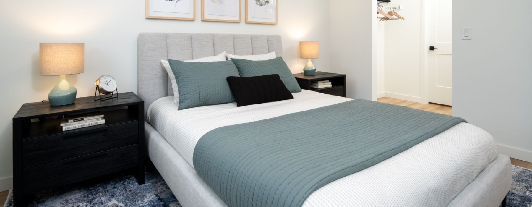 Modern bedroom with a padded bed, blue-gray bedding, matching nightstands, and framed wall art.